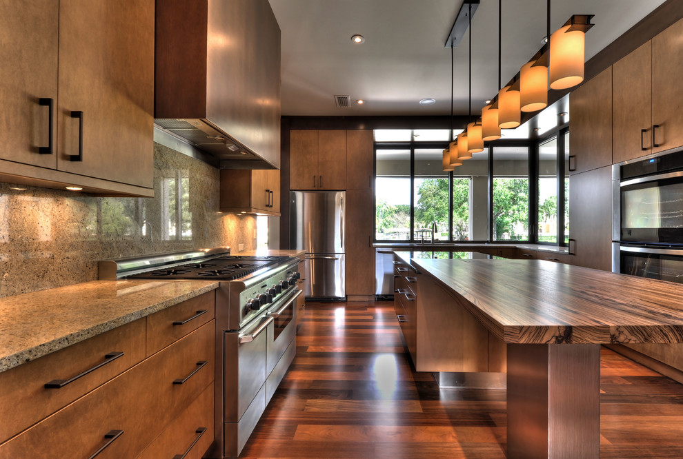 Large modern u-shaped enclosed kitchen in Houston with a submerged sink, flat-panel cabinets, medium wood cabinets, granite worktops, stone slab splashback, stainless steel appliances, laminate floors, an island and brown floors.