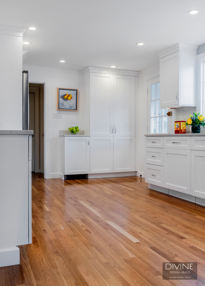 This is an example of a medium sized classic l-shaped kitchen/diner in Boston with a submerged sink, recessed-panel cabinets, white cabinets, engineered stone countertops, grey splashback, ceramic splashback, stainless steel appliances, light hardwood flooring, a breakfast bar and brown floors.