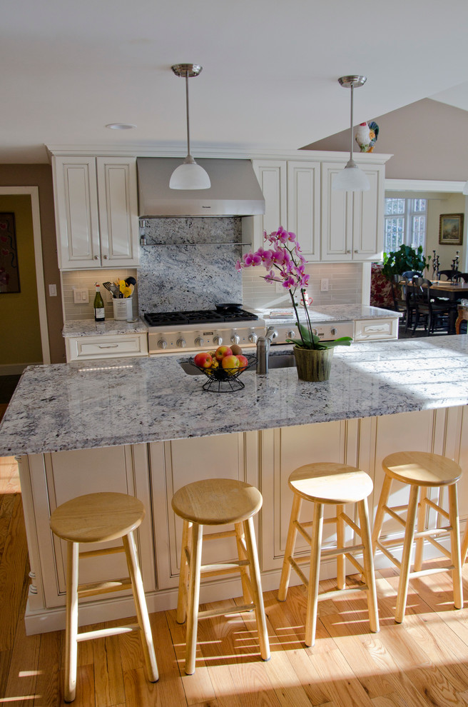 Example of a classic enclosed kitchen design in Boston with a single-bowl sink, raised-panel cabinets, white cabinets, granite countertops, beige backsplash, ceramic backsplash and stainless steel appliances