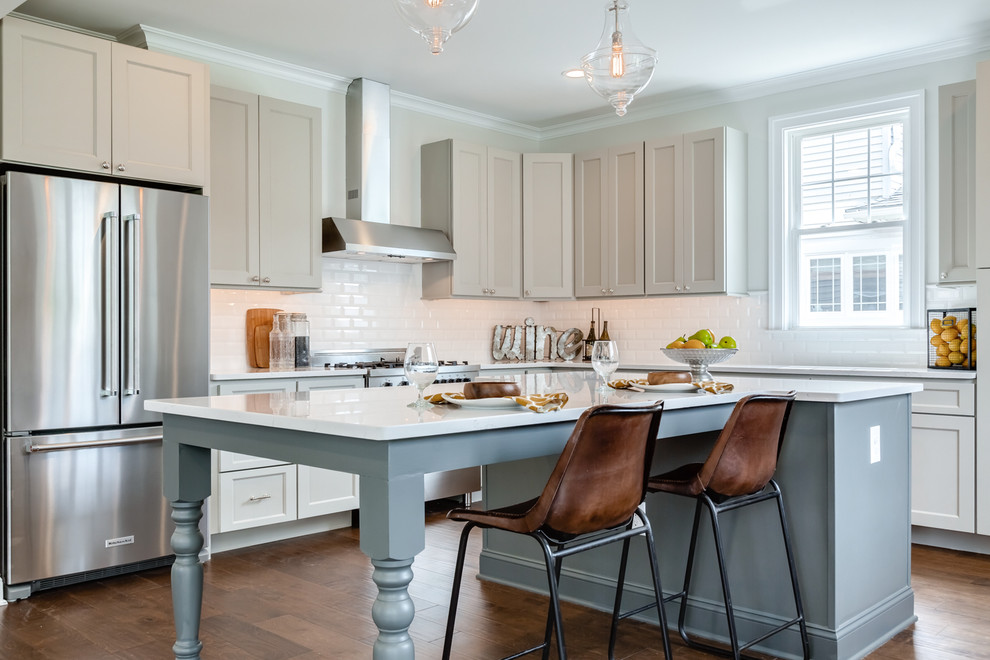 Inspiration for a timeless l-shaped dark wood floor and brown floor kitchen remodel in Philadelphia with shaker cabinets, beige cabinets, white backsplash, subway tile backsplash, stainless steel appliances, an island and white countertops