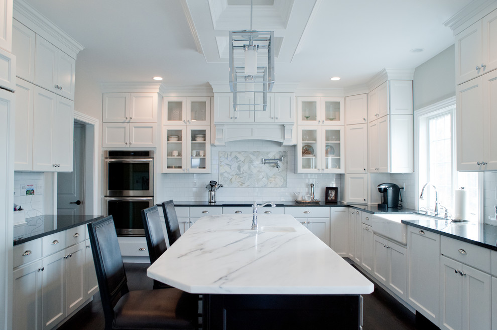 Example of a trendy eat-in kitchen design in New York with a farmhouse sink, glass-front cabinets, white cabinets, marble countertops, white backsplash, subway tile backsplash and stainless steel appliances