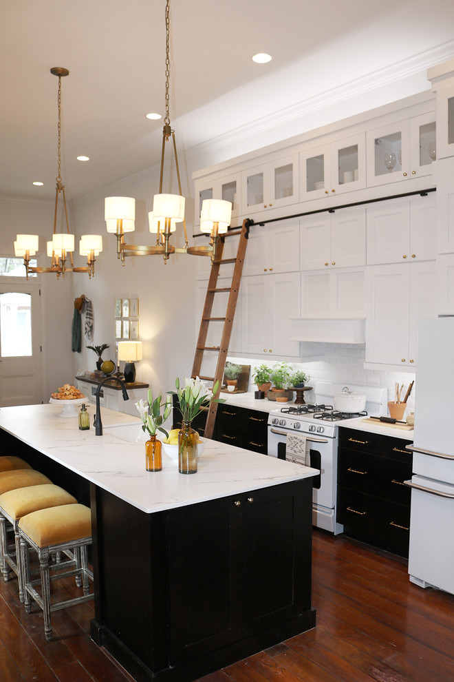 Open concept kitchen - mid-sized transitional l-shaped dark wood floor and brown floor open concept kitchen idea in Other with a farmhouse sink, shaker cabinets, white cabinets, quartzite countertops, white backsplash, subway tile backsplash, white appliances and an island