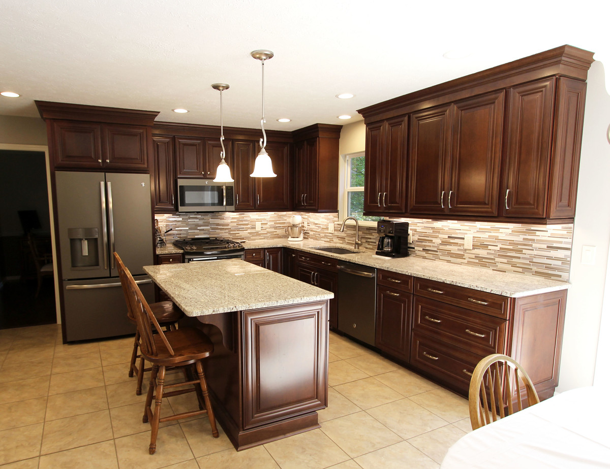 Inspiration for a mid-sized timeless l-shaped ceramic tile and beige floor eat-in kitchen remodel in Cleveland with an undermount sink, raised-panel cabinets, dark wood cabinets, granite countertops, brown backsplash, glass tile backsplash, stainless steel appliances and an island