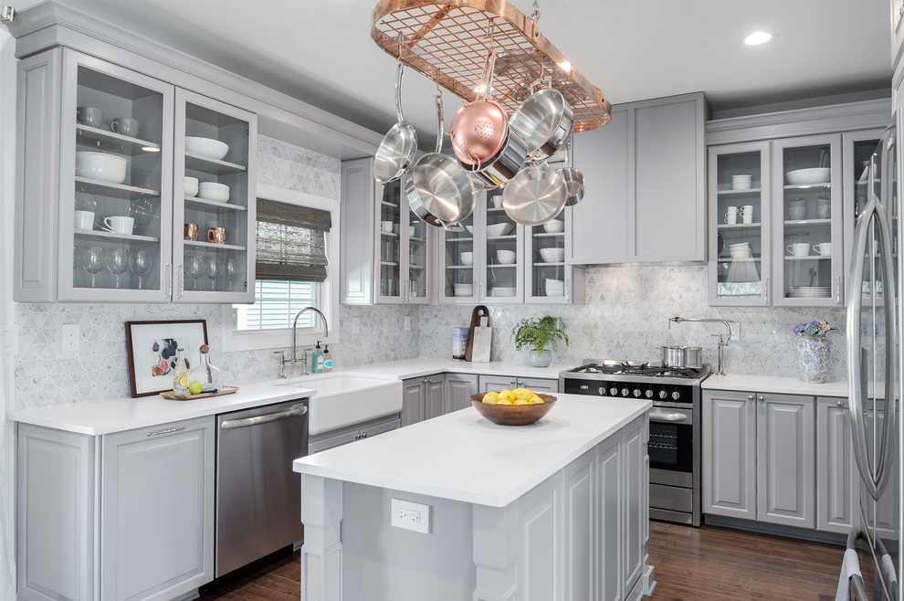 Foto de cocinas en U tradicional con fregadero sobremueble, armarios con paneles con relieve, puertas de armario grises, salpicadero blanco, electrodomésticos de acero inoxidable, suelo de madera oscura, una isla y suelo marrón