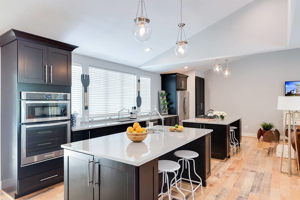 Large trendy single-wall light wood floor and beige floor open concept kitchen photo in Providence with an undermount sink, recessed-panel cabinets, brown cabinets, solid surface countertops, stainless steel appliances, two islands and white countertops
