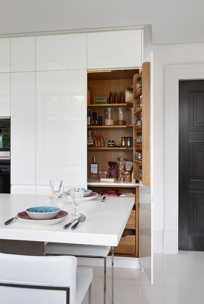 Photo of a large modern grey and cream u-shaped open plan kitchen in London with an integrated sink, flat-panel cabinets, white cabinets, composite countertops, integrated appliances, ceramic flooring, an island, white floors and white worktops.