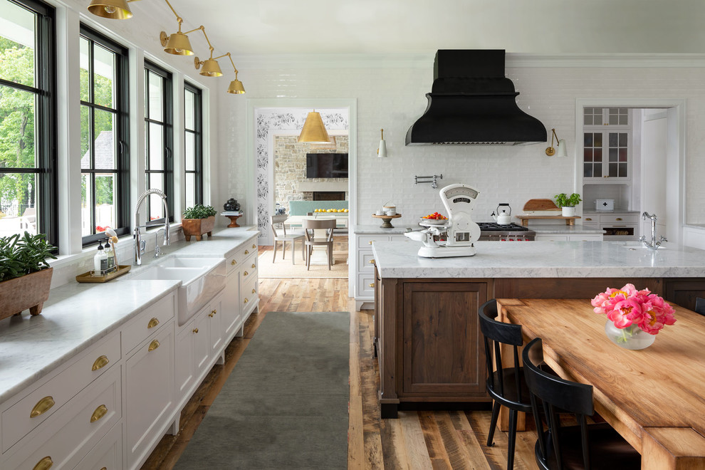 Example of a beach style medium tone wood floor eat-in kitchen design in Minneapolis with a farmhouse sink, shaker cabinets, white cabinets, marble countertops, white backsplash, stainless steel appliances, an island and white countertops