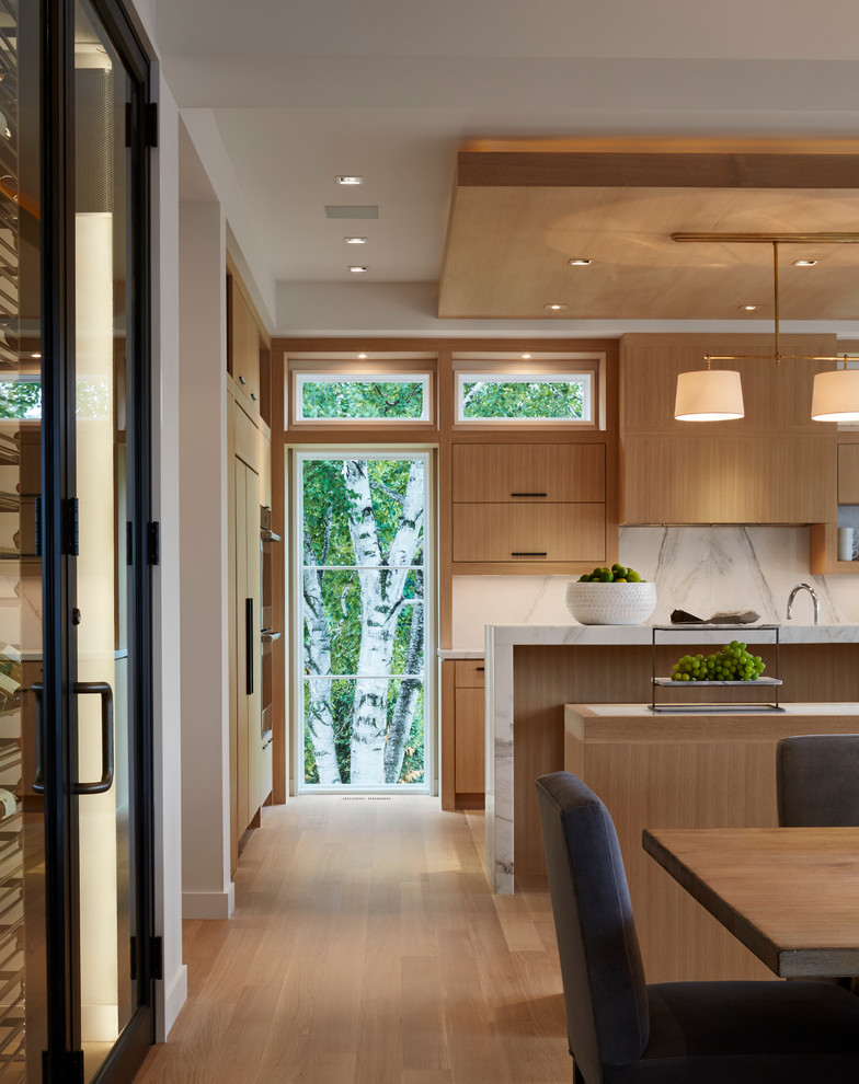 Eat-in kitchen - modern light wood floor eat-in kitchen idea in Minneapolis with flat-panel cabinets, light wood cabinets, marble countertops, white backsplash, stone slab backsplash, paneled appliances and two islands