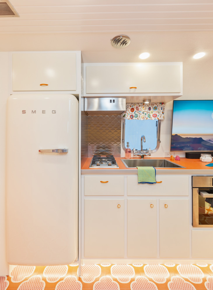Diseño de cocina bohemia pequeña con armarios con paneles lisos, puertas de armario blancas, encimera de laminado, salpicadero metalizado, electrodomésticos blancos, suelo de madera pintada, suelo naranja y encimeras naranjas