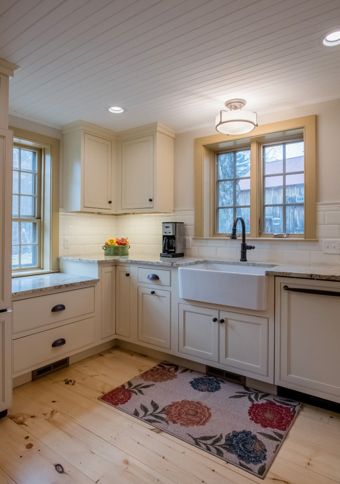 ボストンにある高級なカントリー風のおしゃれなダイニングキッチン (エプロンフロントシンク、インセット扉のキャビネット、白いキャビネット、御影石カウンター、白いキッチンパネル、磁器タイルのキッチンパネル、シルバーの調理設備、淡色無垢フローリング、アイランドなし、茶色い床、ベージュのキッチンカウンター) の写真