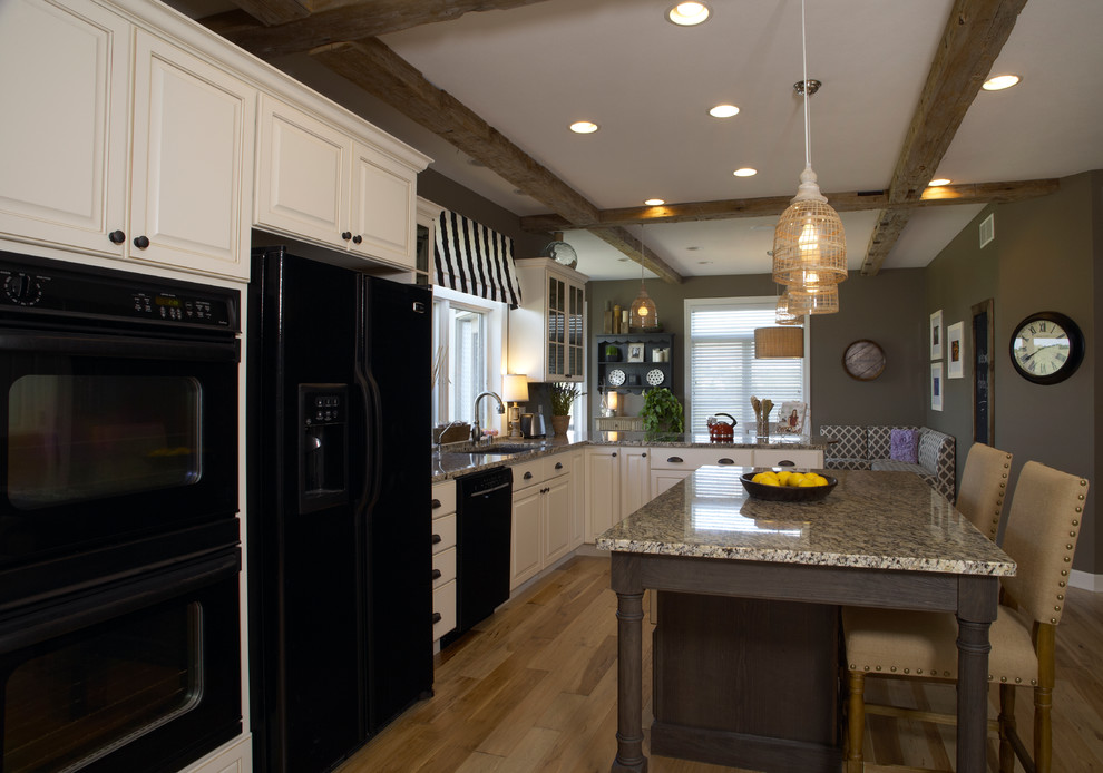 Offene Urige Küche in L-Form mit Unterbauwaschbecken, profilierten Schrankfronten, weißen Schränken, Granit-Arbeitsplatte, schwarzen Elektrogeräten, hellem Holzboden und Kücheninsel in Milwaukee