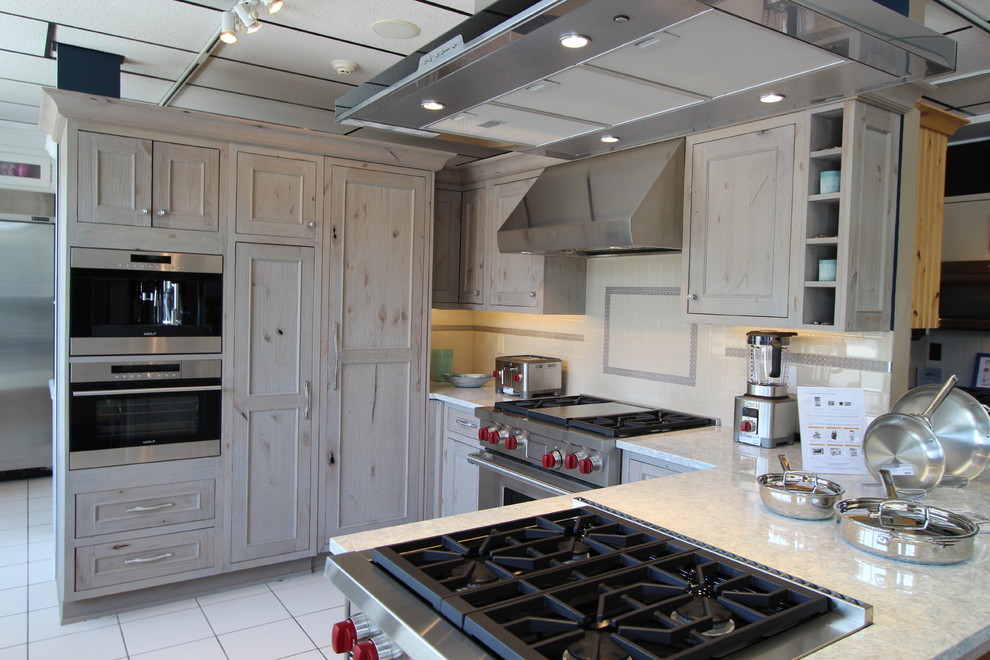Bild på ett mellanstort maritimt kök, med en undermonterad diskho, luckor med infälld panel, skåp i slitet trä, bänkskiva i kvarts, blått stänkskydd, stänkskydd i tunnelbanekakel, rostfria vitvaror, klinkergolv i keramik och en halv köksö