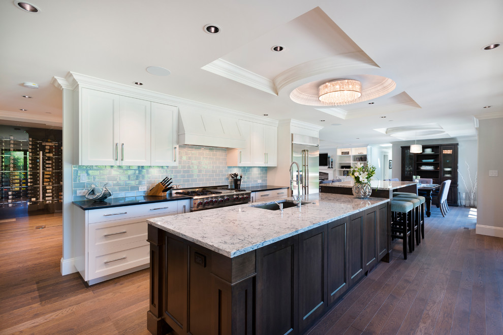 Large transitional l-shaped medium tone wood floor open concept kitchen photo in Vancouver with an undermount sink, shaker cabinets, white cabinets, quartz countertops, blue backsplash, subway tile backsplash, stainless steel appliances and an island