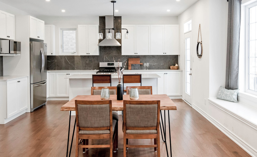 Klassische Wohnküche in L-Form mit Schrankfronten im Shaker-Stil, weißen Schränken, Küchenrückwand in Grau, Küchengeräten aus Edelstahl, braunem Holzboden, Kücheninsel, weißer Arbeitsplatte und Rückwand aus Schiefer in Toronto