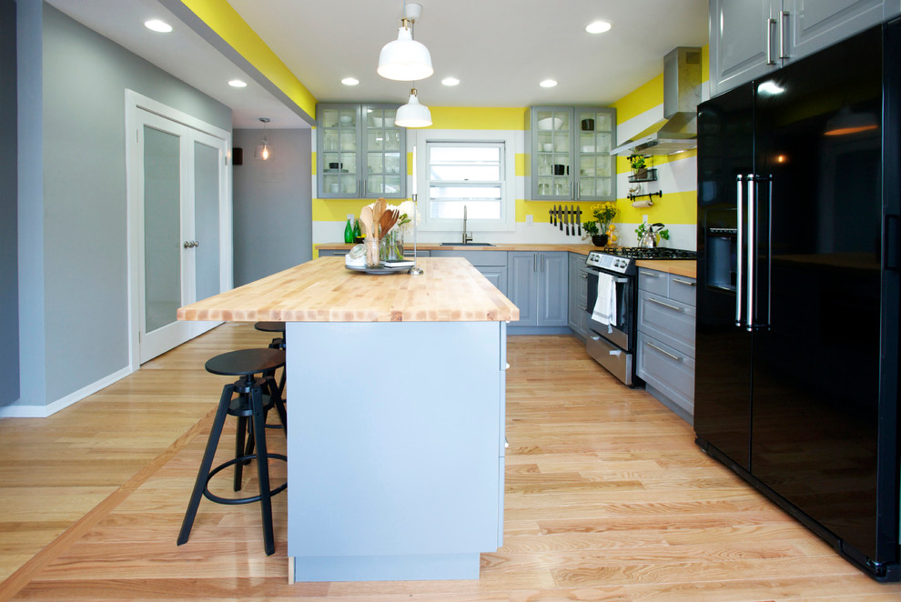 Bild på ett funkis kök, med en nedsänkt diskho, luckor med upphöjd panel, grå skåp, träbänkskiva, svarta vitvaror, mellanmörkt trägolv och en köksö