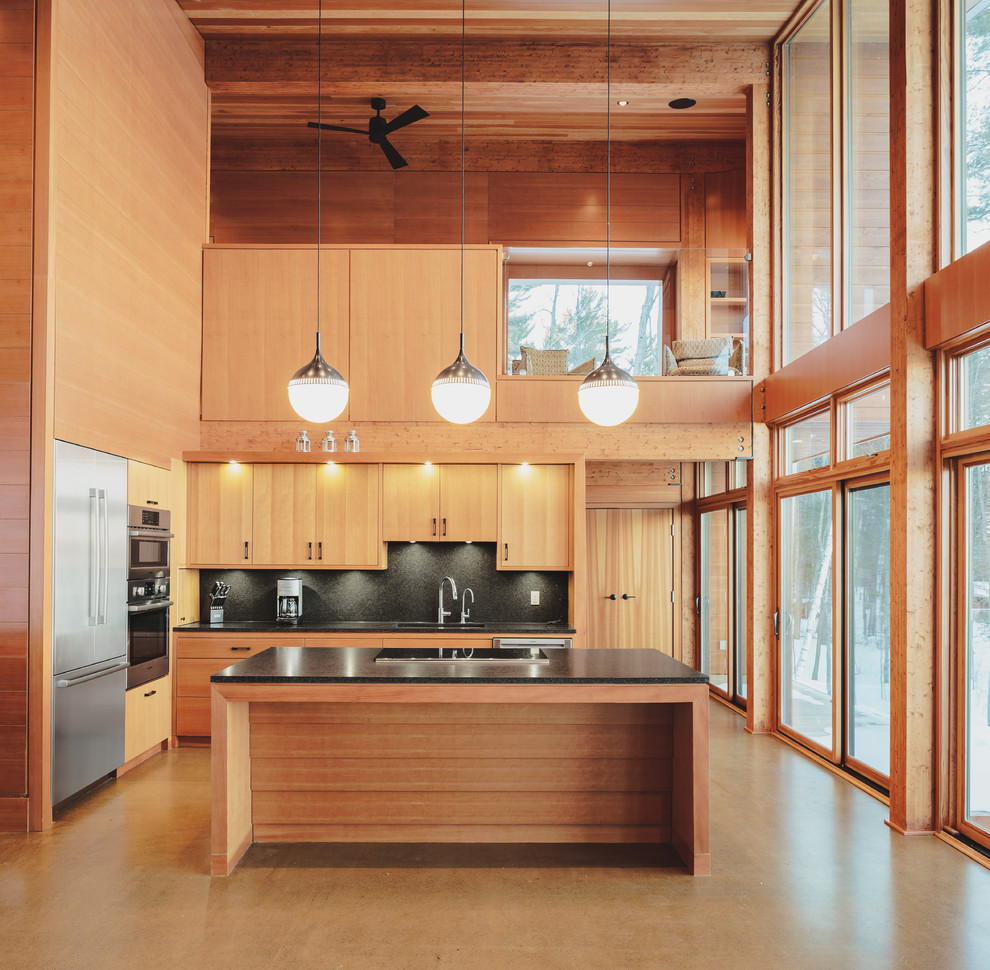 Bild på ett stort funkis l-kök, med luckor med infälld panel, skåp i ljust trä, svart stänkskydd, rostfria vitvaror och en köksö