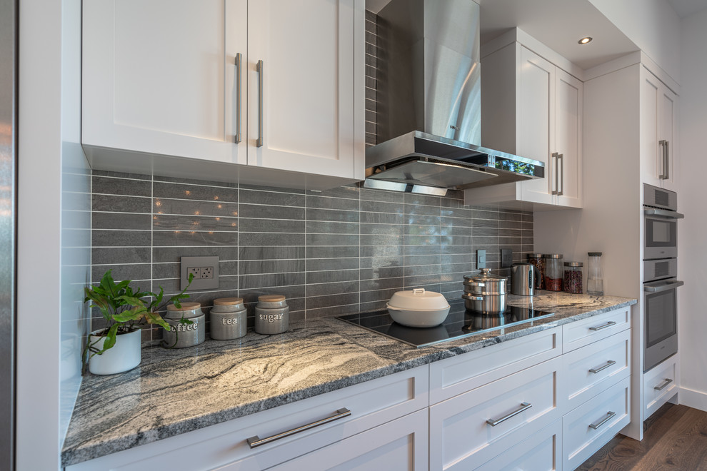 This is an example of a medium sized modern single-wall open plan kitchen in Other with a submerged sink, shaker cabinets, white cabinets, grey splashback, metro tiled splashback, stainless steel appliances, medium hardwood flooring, an island, brown floors and grey worktops.