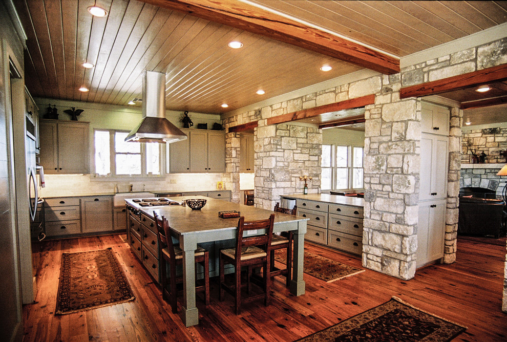Inspiration for a large cottage u-shaped medium tone wood floor eat-in kitchen remodel in Houston with a farmhouse sink, an island, recessed-panel cabinets, gray cabinets, granite countertops, beige backsplash, stone tile backsplash and stainless steel appliances