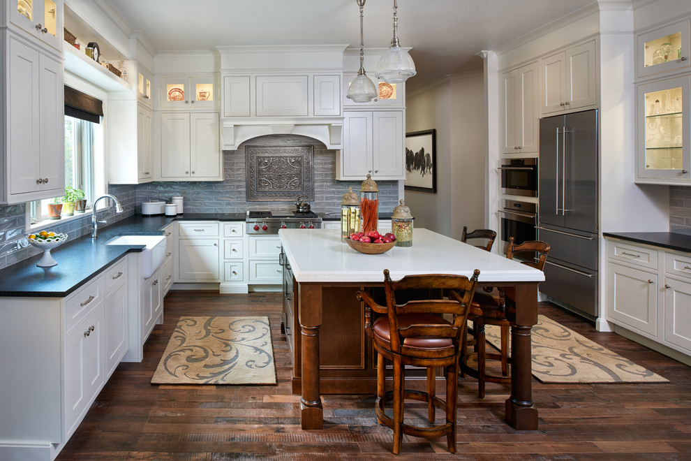 Bild på ett avskilt, stort vintage u-kök, med en rustik diskho, luckor med profilerade fronter, vita skåp, bänkskiva i kvarts, grått stänkskydd, stänkskydd i porslinskakel, rostfria vitvaror, mellanmörkt trägolv och en köksö