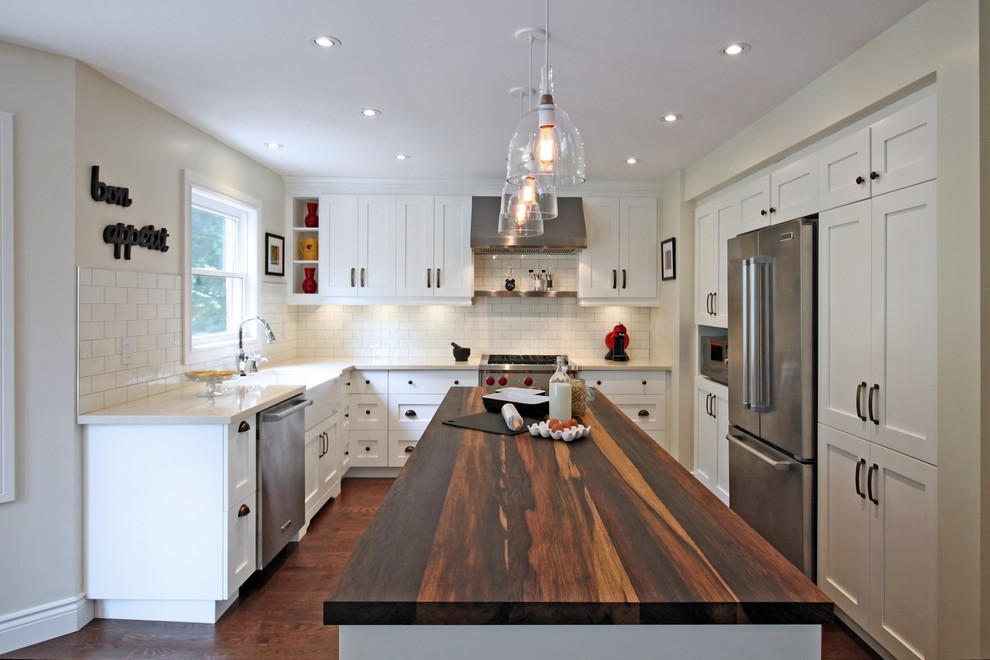 This is an example of a small eclectic l-shaped kitchen in Toronto with a belfast sink, wood worktops, white splashback, stainless steel appliances, medium hardwood flooring and an island.