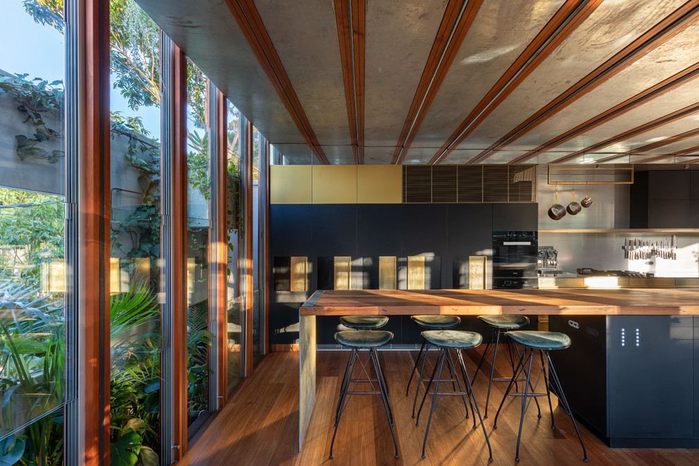 Zweizeilige Moderne Küche mit flächenbündigen Schrankfronten, schwarzen Schränken, Arbeitsplatte aus Holz, Küchenrückwand in Grau, braunem Holzboden, Kücheninsel, braunem Boden und brauner Arbeitsplatte in Sydney