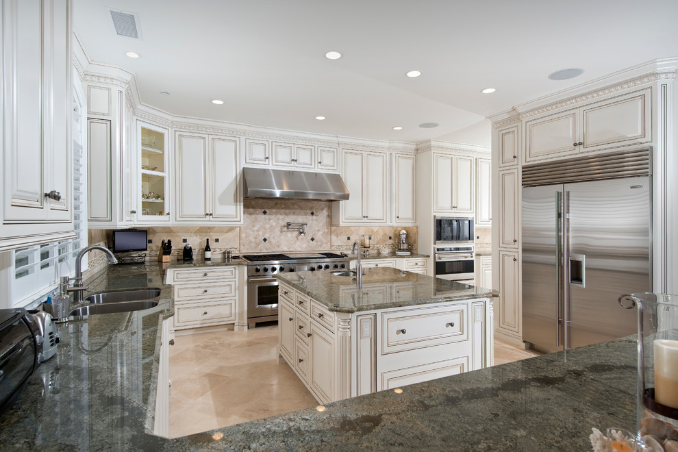 Photo of a large traditional u-shaped kitchen/diner in Orange County with a submerged sink, raised-panel cabinets, white cabinets, granite worktops, beige splashback, stone tiled splashback, stainless steel appliances, marble flooring, an island and beige floors.