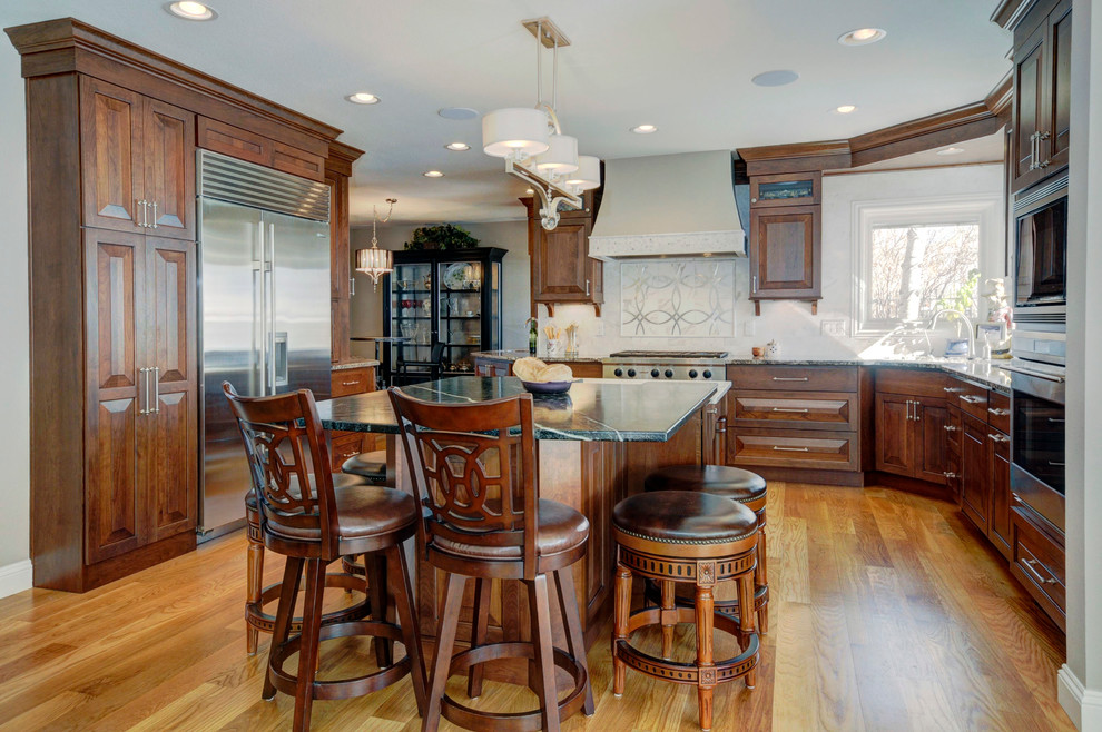 Eat-in kitchen - mid-sized traditional light wood floor eat-in kitchen idea in Denver with an undermount sink, raised-panel cabinets, dark wood cabinets, solid surface countertops, white backsplash, subway tile backsplash and white appliances
