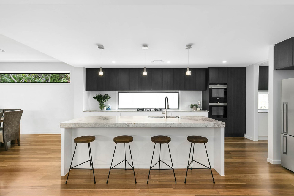 Inredning av ett modernt stort grå grått kök, med en undermonterad diskho, skåp i mörkt trä, marmorbänkskiva, vitt stänkskydd, stänkskydd i keramik, svarta vitvaror, mellanmörkt trägolv, en köksö och brunt golv