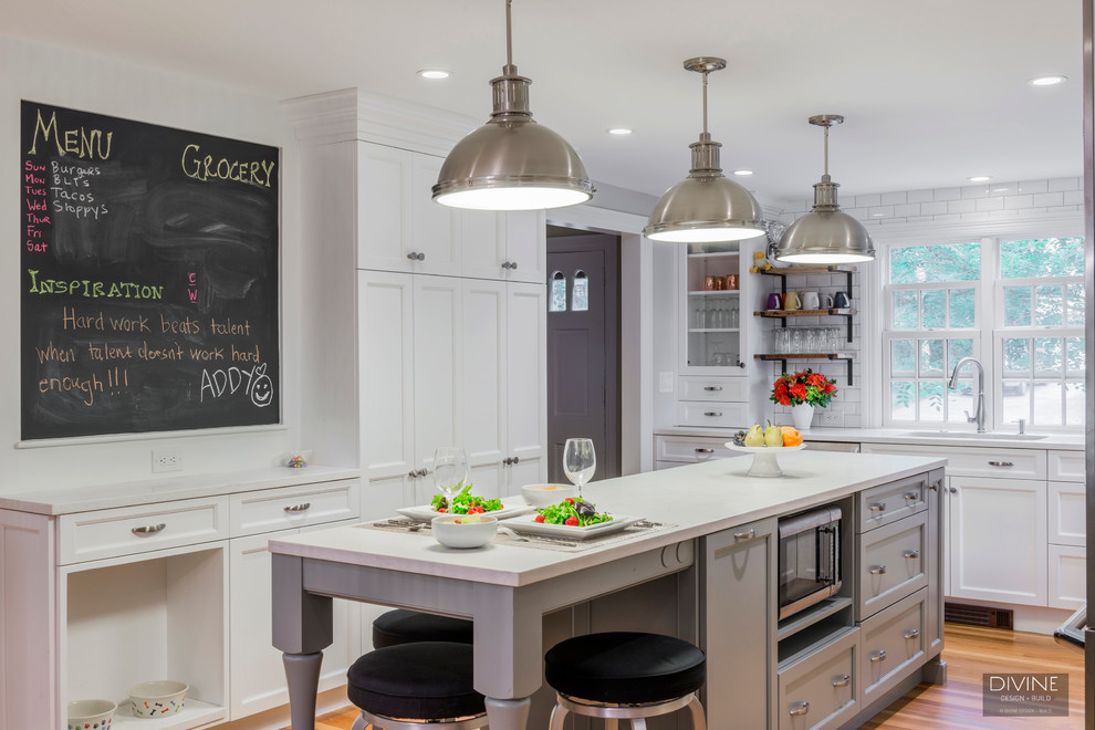 Example of a mid-sized transitional galley medium tone wood floor and brown floor eat-in kitchen design in Boston with an undermount sink, shaker cabinets, white cabinets, white backsplash, subway tile backsplash, stainless steel appliances, an island and quartz countertops