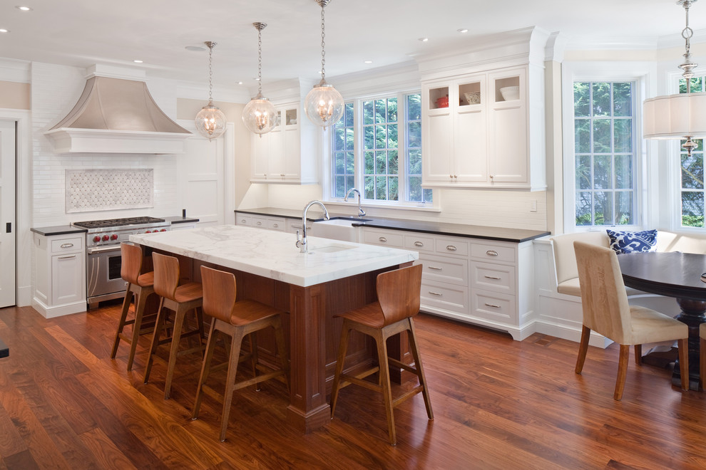 Classic l-shaped kitchen in Boston with a belfast sink, recessed-panel cabinets, white cabinets, white splashback, stainless steel appliances, dark hardwood flooring and an island.