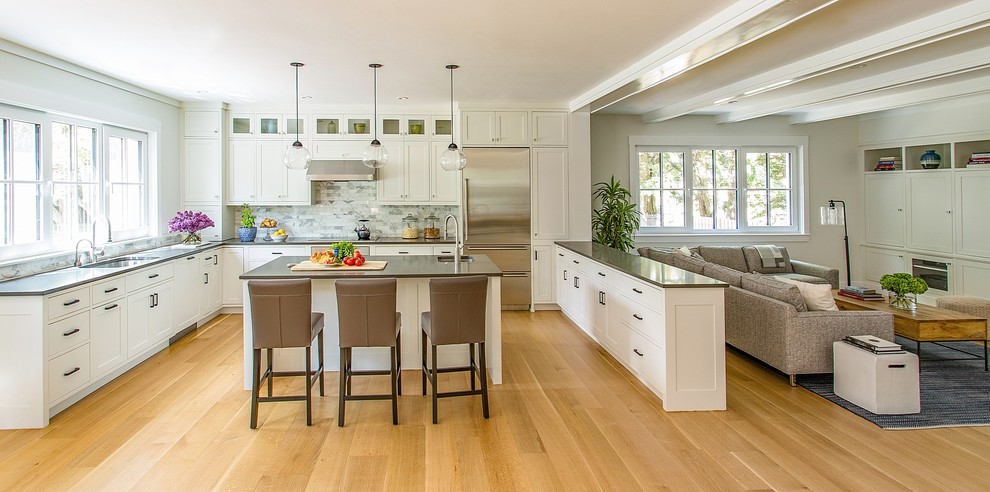 This is an example of a medium sized contemporary u-shaped open plan kitchen in Boston with a submerged sink, shaker cabinets, white cabinets, engineered stone countertops, grey splashback, marble splashback, stainless steel appliances, medium hardwood flooring, an island and brown floors.