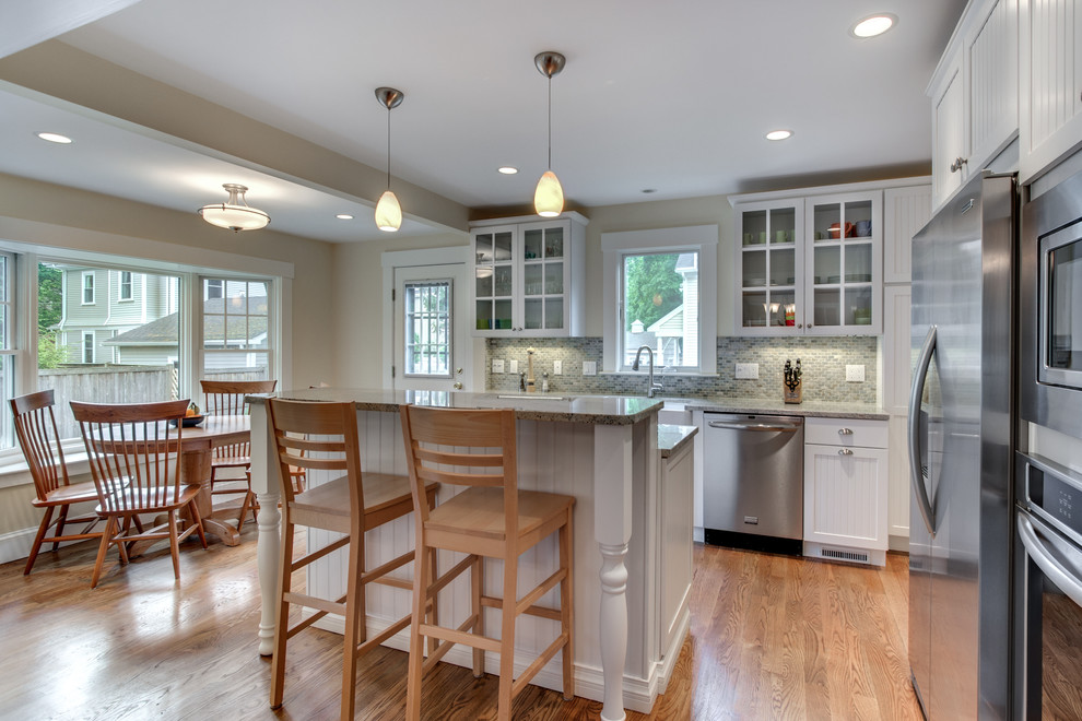 Eat-in kitchen - mid-sized traditional l-shaped eat-in kitchen idea in Boston with a farmhouse sink, louvered cabinets, white cabinets, granite countertops, multicolored backsplash, subway tile backsplash, stainless steel appliances and an island