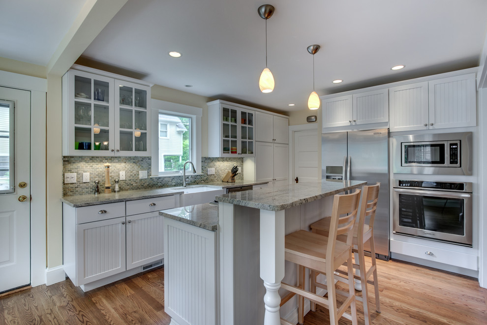 Eat-in kitchen - mid-sized traditional l-shaped medium tone wood floor eat-in kitchen idea in Boston with a farmhouse sink, louvered cabinets, white cabinets, granite countertops, multicolored backsplash, subway tile backsplash, stainless steel appliances and an island