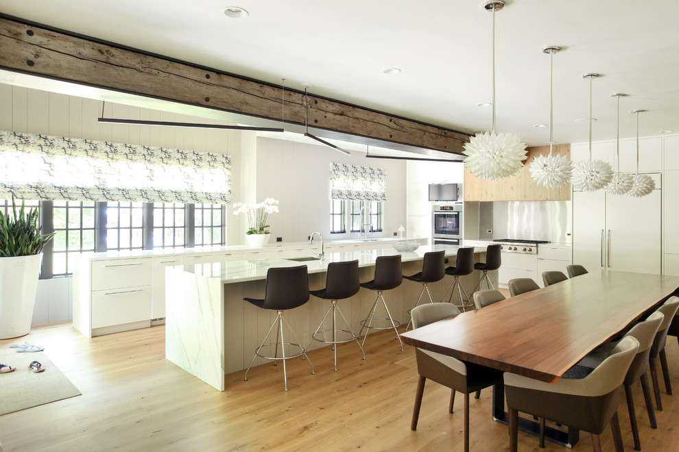 Moderne Wohnküche mit flächenbündigen Schrankfronten, weißen Schränken, Elektrogeräten mit Frontblende, braunem Holzboden und Kücheninsel in New York