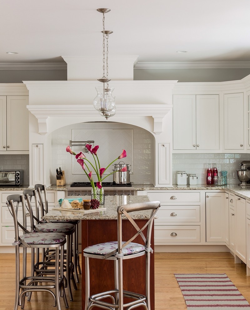 Photo of a classic l-shaped kitchen in Boston with beaded cabinets, white cabinets, white splashback, metro tiled splashback, stainless steel appliances, medium hardwood flooring and an island.