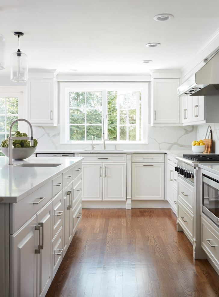This is an example of a large contemporary kitchen/diner in Boston with a built-in sink, white cabinets, quartz worktops, white splashback, stainless steel appliances, dark hardwood flooring, an island and brown floors.