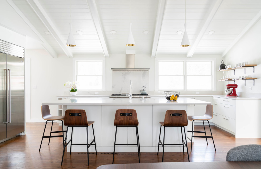 Inredning av ett modernt vit vitt kök, med släta luckor, vita skåp, rostfria vitvaror, mellanmörkt trägolv, en köksö och brunt golv