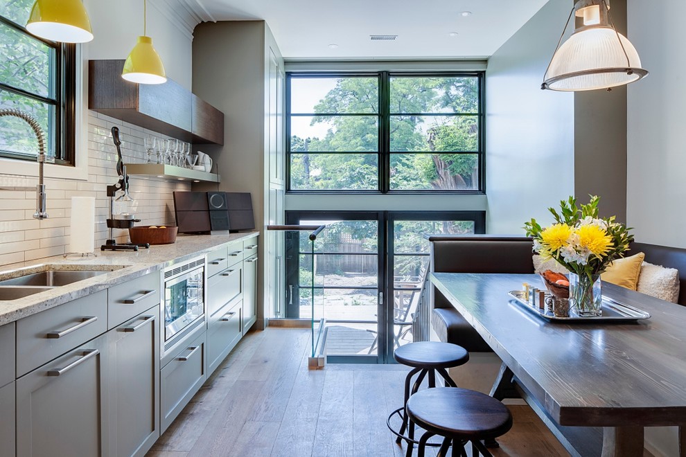 Inspiration for a mid-sized contemporary l-shaped light wood floor eat-in kitchen remodel in Toronto with green cabinets, shaker cabinets, white backsplash, subway tile backsplash, a double-bowl sink, granite countertops, stainless steel appliances and no island