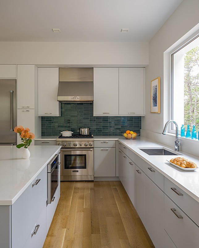 Mid-sized minimalist l-shaped open concept kitchen photo in Boston with flat-panel cabinets, gray cabinets, quartz countertops, white backsplash, stainless steel appliances and an island