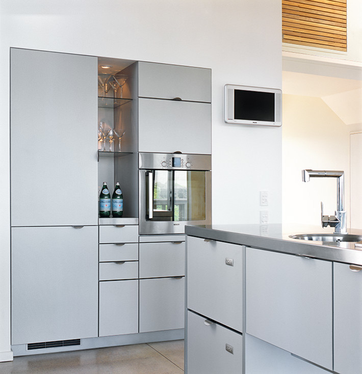 Moderne Küche in L-Form mit Vorratsschrank, Waschbecken, grauen Schränken, Edelstahl-Arbeitsplatte, Küchengeräten aus Edelstahl, Betonboden und Kücheninsel in Wellington