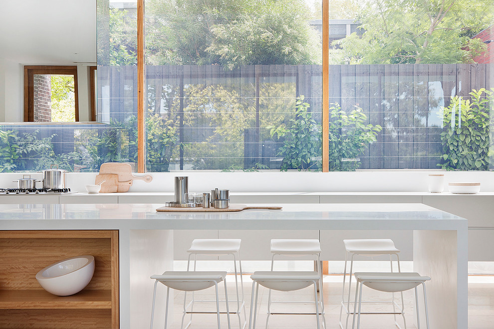 Imagen de cocina minimalista con una isla, armarios con paneles lisos, puertas de armario blancas, salpicadero de vidrio templado y electrodomésticos de acero inoxidable