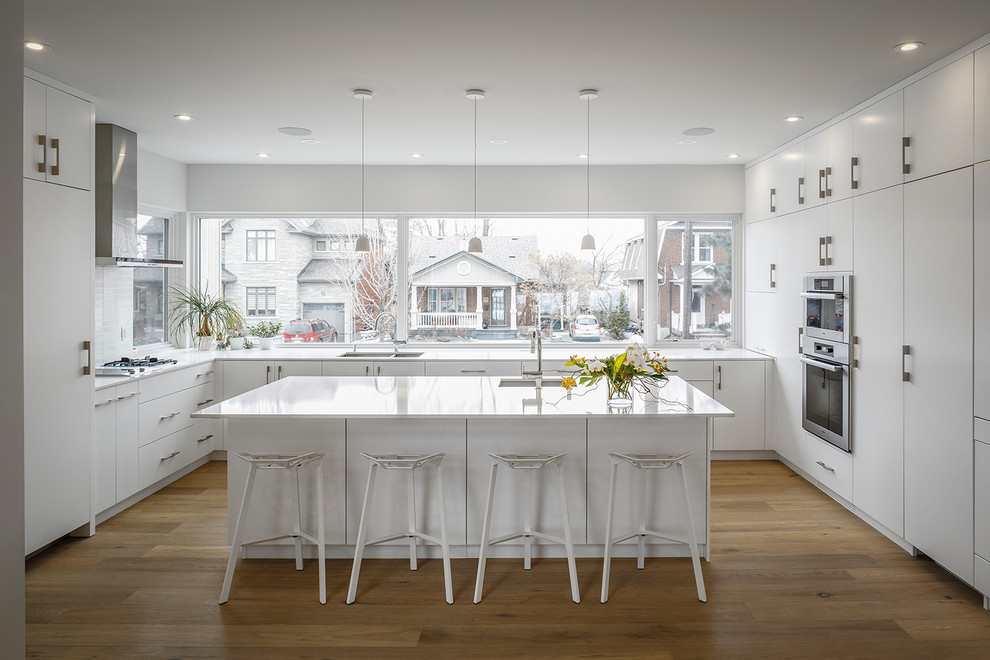 Moderne Küche mit flächenbündigen Schrankfronten, weißen Schränken, Granit-Arbeitsplatte, Kücheninsel, Unterbauwaschbecken, Küchengeräten aus Edelstahl und braunem Holzboden in Ottawa