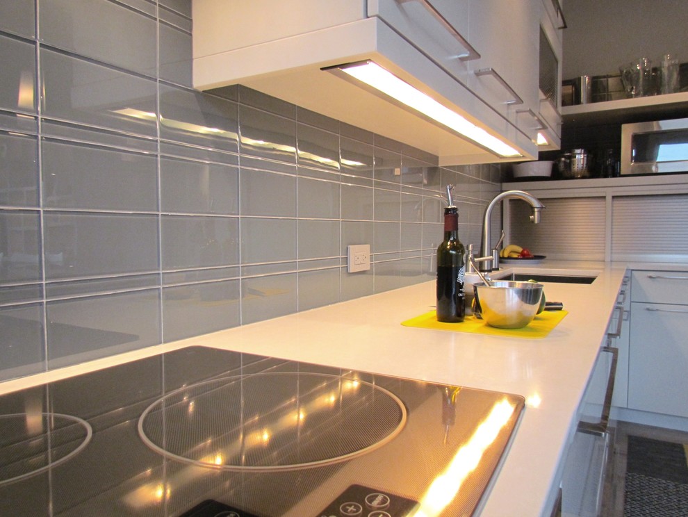 This is an example of a medium sized contemporary l-shaped kitchen/diner in Chicago with a submerged sink, flat-panel cabinets, white cabinets, engineered stone countertops, grey splashback, glass tiled splashback, integrated appliances, light hardwood flooring, an island and brown floors.