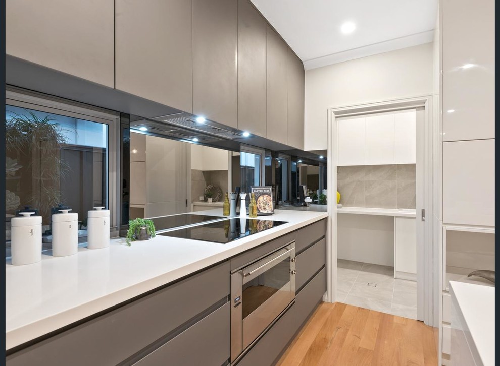 Bild på ett mellanstort funkis kök, med en undermonterad diskho, släta luckor, vita skåp, bänkskiva i kvarts, stänkskydd med metallisk yta, spegel som stänkskydd, rostfria vitvaror, ljust trägolv och en köksö