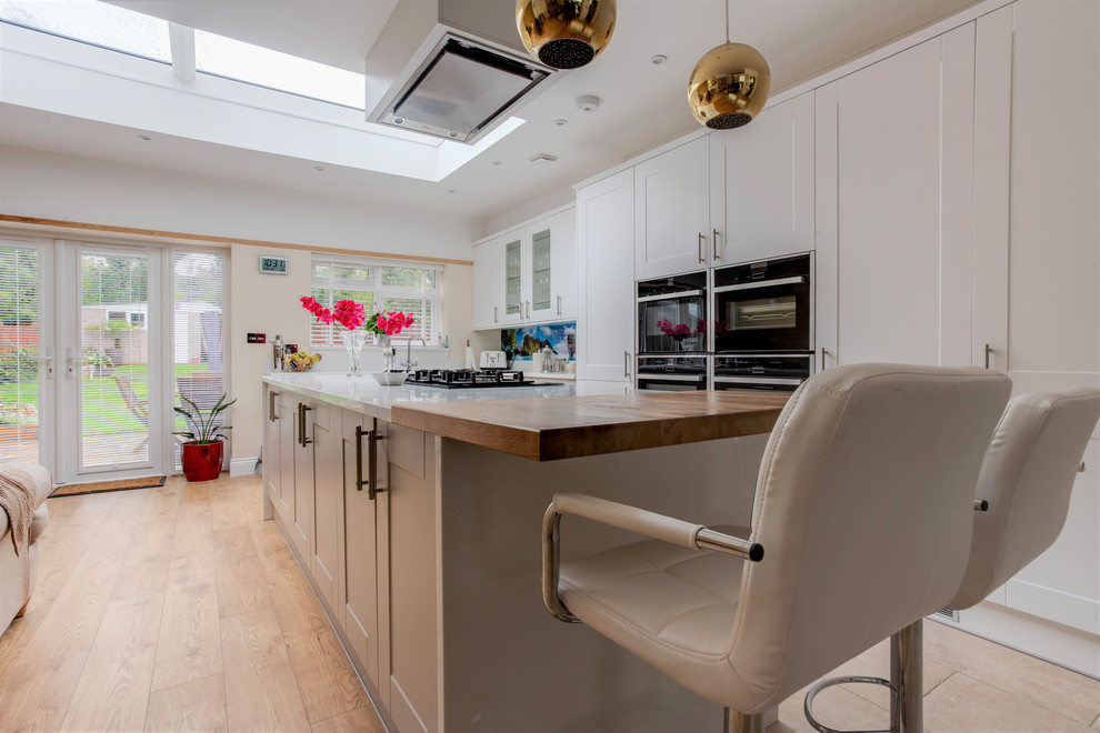 Inspiration for a medium sized contemporary open plan kitchen in London with white worktops, a built-in sink, recessed-panel cabinets, white cabinets, glass sheet splashback, integrated appliances, an island and beige floors.