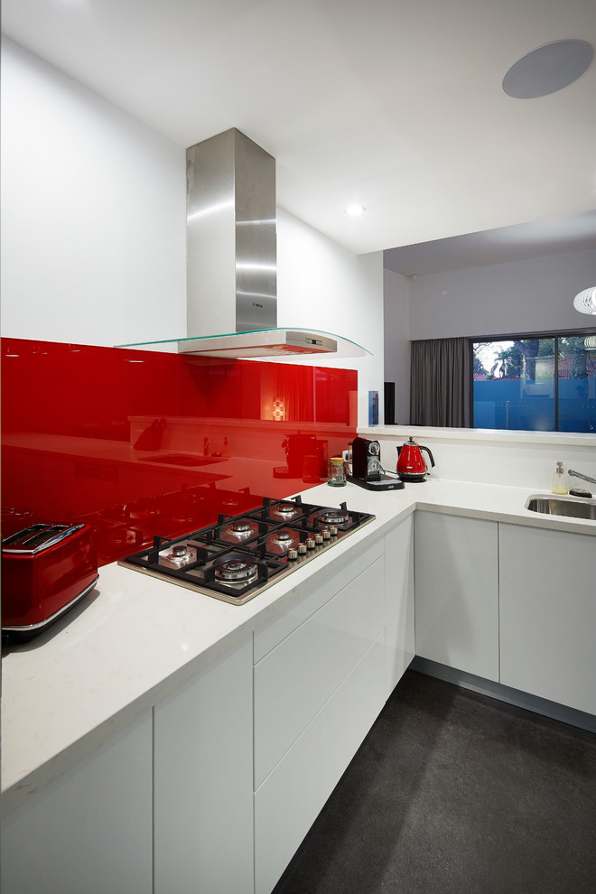 Mittelgroße Moderne Wohnküche ohne Insel in U-Form mit weißen Schränken, Quarzwerkstein-Arbeitsplatte, Küchenrückwand in Rot, Glasrückwand, Küchengeräten aus Edelstahl und Betonboden in Perth