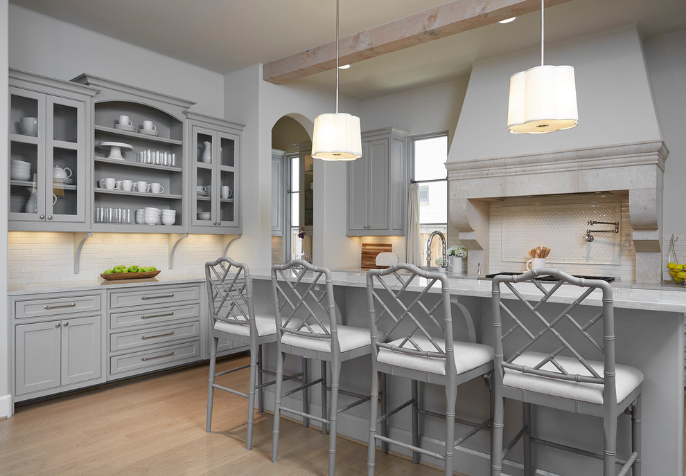 Mediterrane Küche mit Kassettenfronten, grauen Schränken, Küchenrückwand in Weiß, hellem Holzboden, Kücheninsel und braunem Boden in Dallas