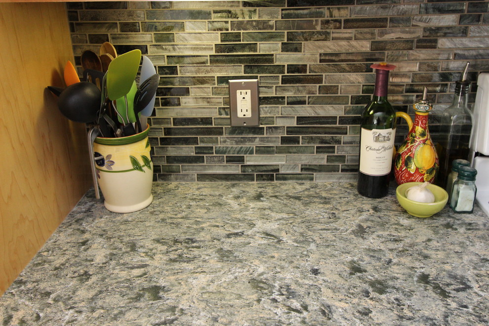 Klassisk inredning av ett mellanstort kök, med en undermonterad diskho, skåp i ljust trä, bänkskiva i kvarts, grönt stänkskydd, stänkskydd i glaskakel, vita vitvaror, linoleumgolv, en halv köksö och luckor med infälld panel
