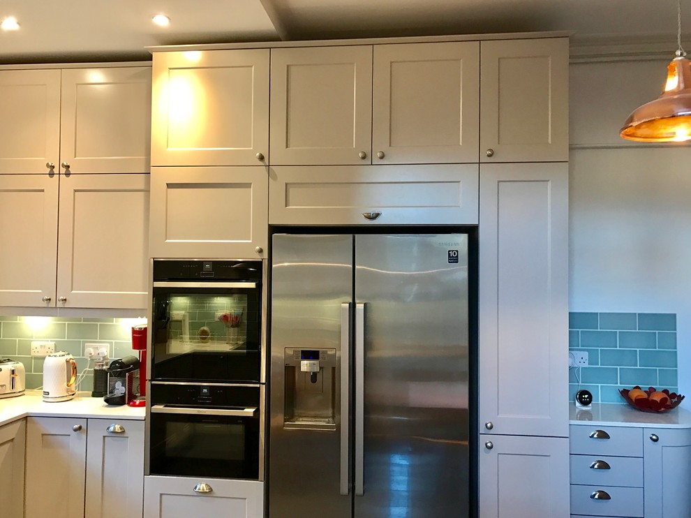 Modern inredning av ett kök och matrum, med en undermonterad diskho, bänkskiva i kvartsit, grönt stänkskydd, stänkskydd i glaskakel, integrerade vitvaror och klinkergolv i porslin