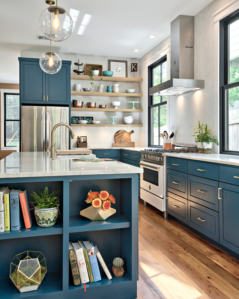 Design ideas for a farmhouse l-shaped kitchen in Austin with a belfast sink, flat-panel cabinets, blue cabinets, white splashback, white appliances, medium hardwood flooring, an island, brown floors and white worktops.